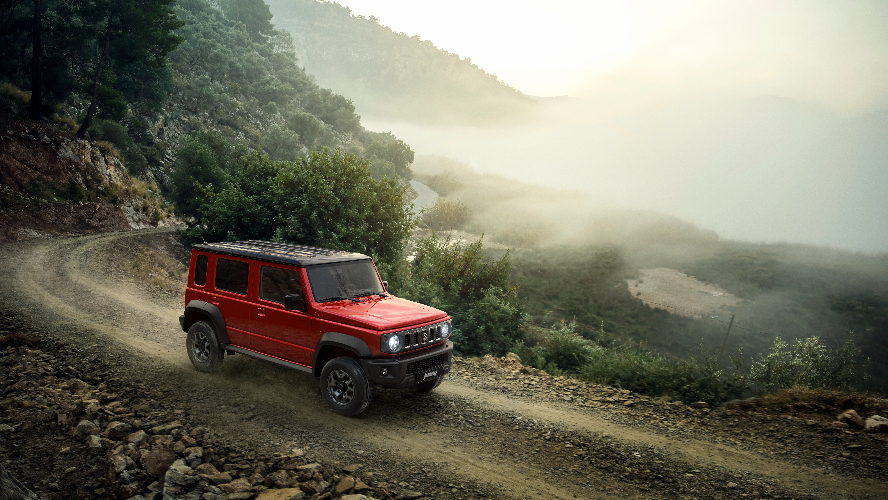A red 5-door Suzuki Jimny driving off-road.